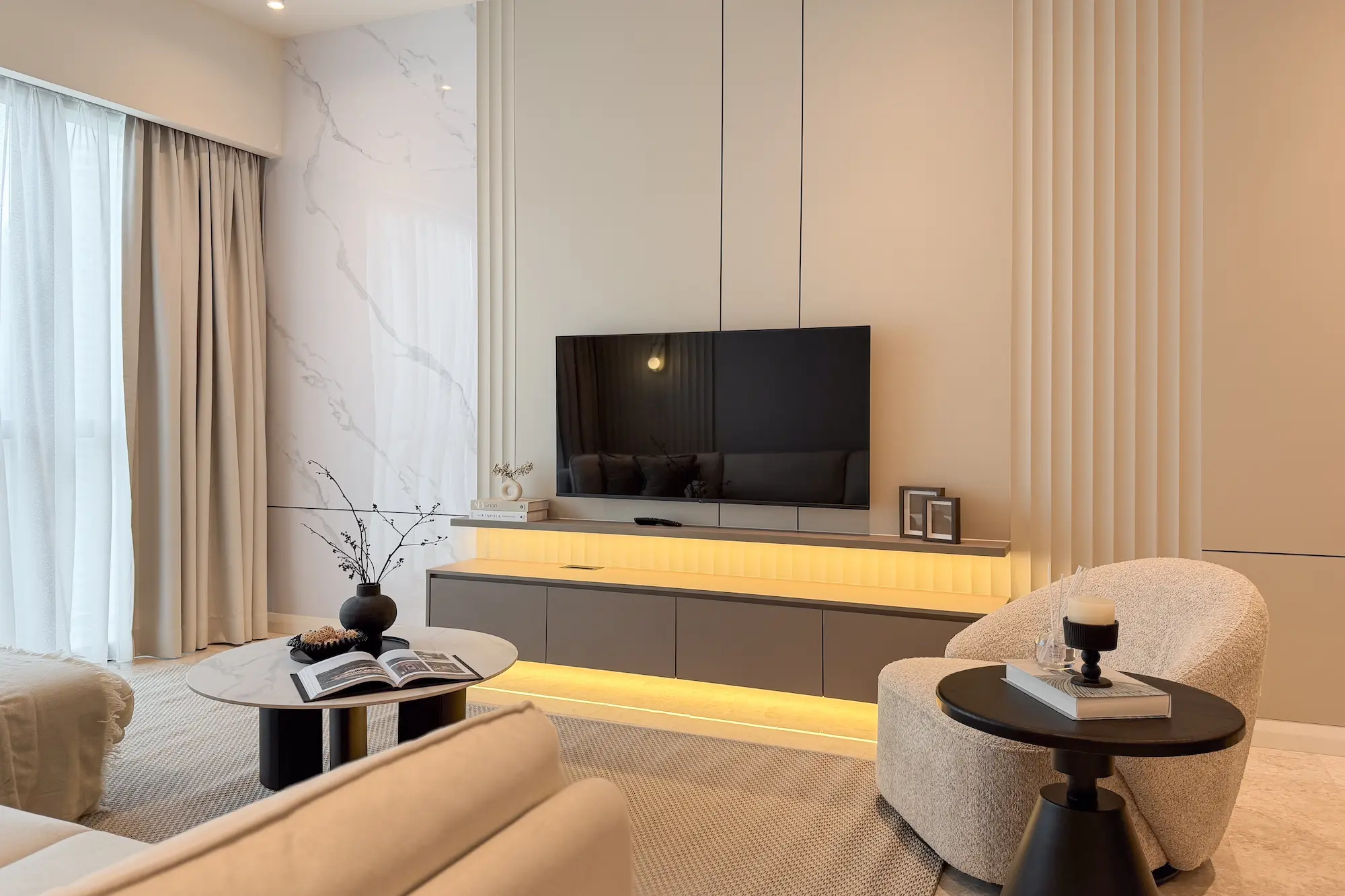 Warm minimalist living room in TRX Residence Kuala Lumpur featuring a marble TV wall, fluted panels, neutral furnishings and layered ambient lighting.