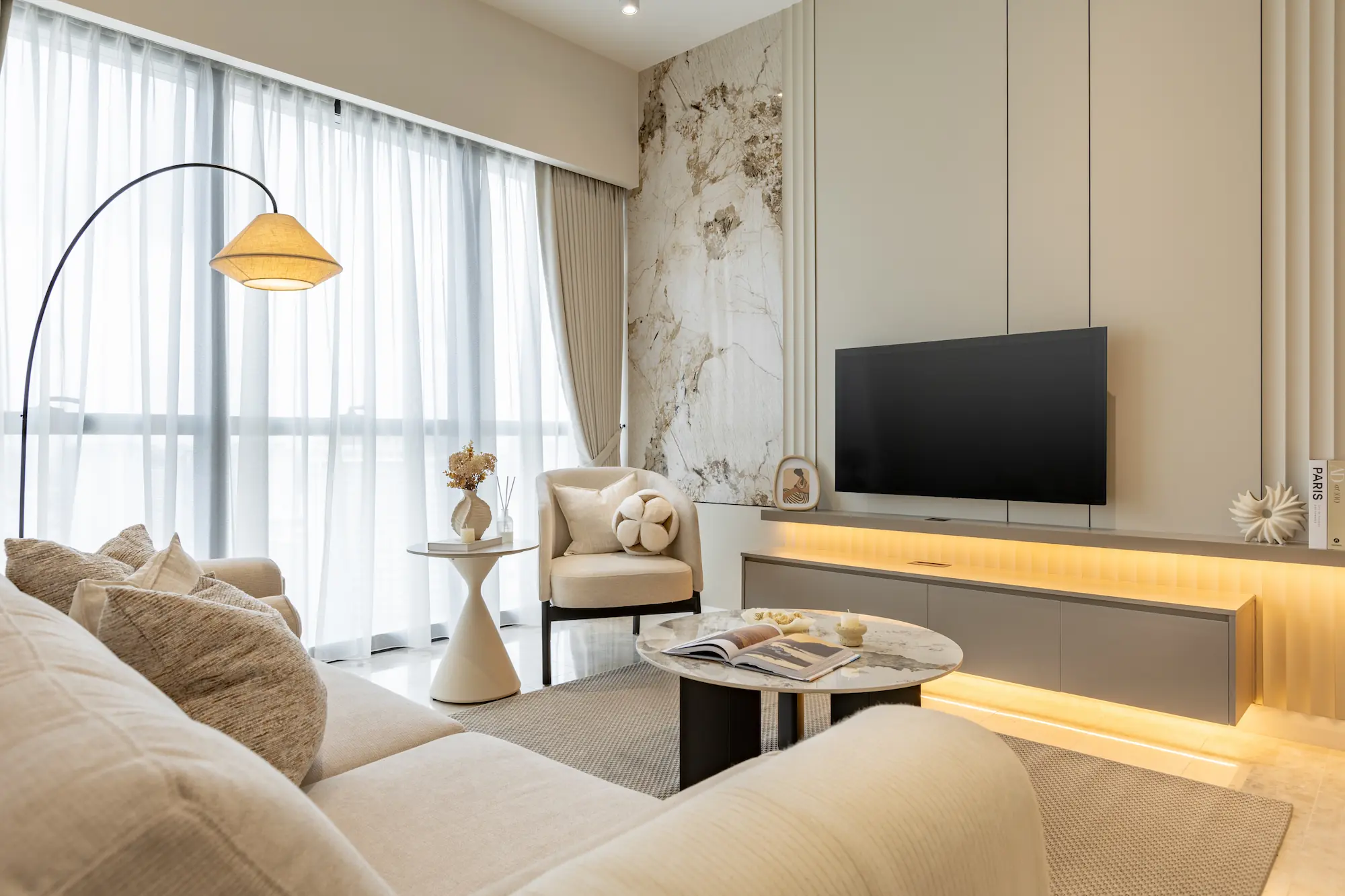 Modern neutral-toned living room interior with marble TV feature wall, built-in cabinetry and warm ambient lighting in TRX Residences Kuala Lumpur