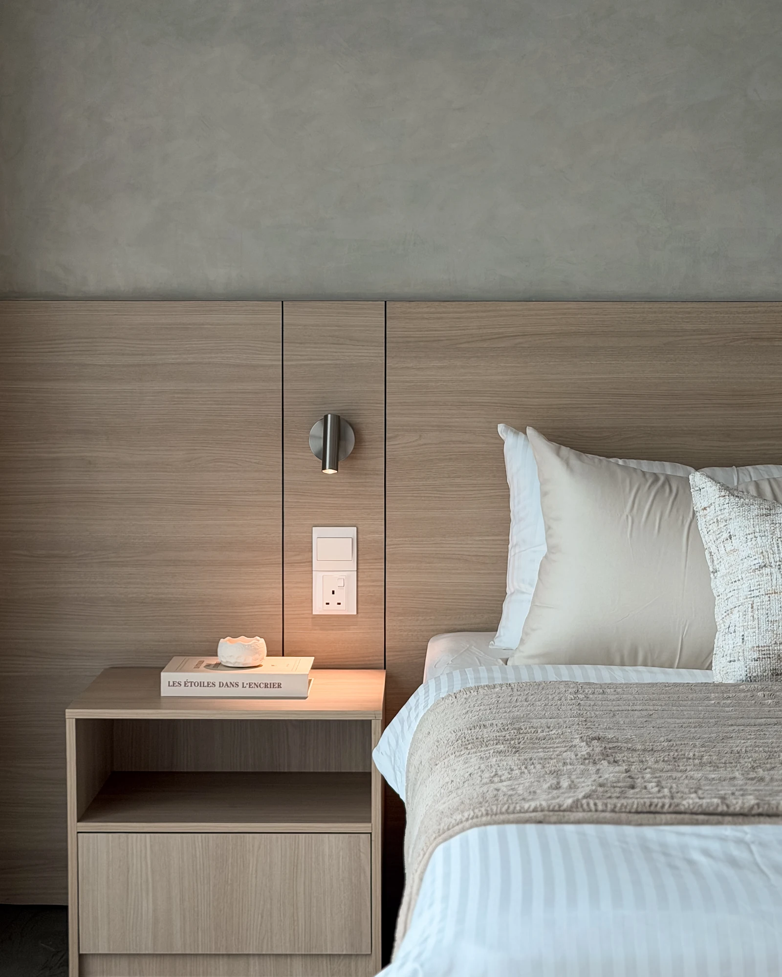 Wood bedside table with integrated reading light and open storage beside the master bed at Ooak Suites, Mont Kiara