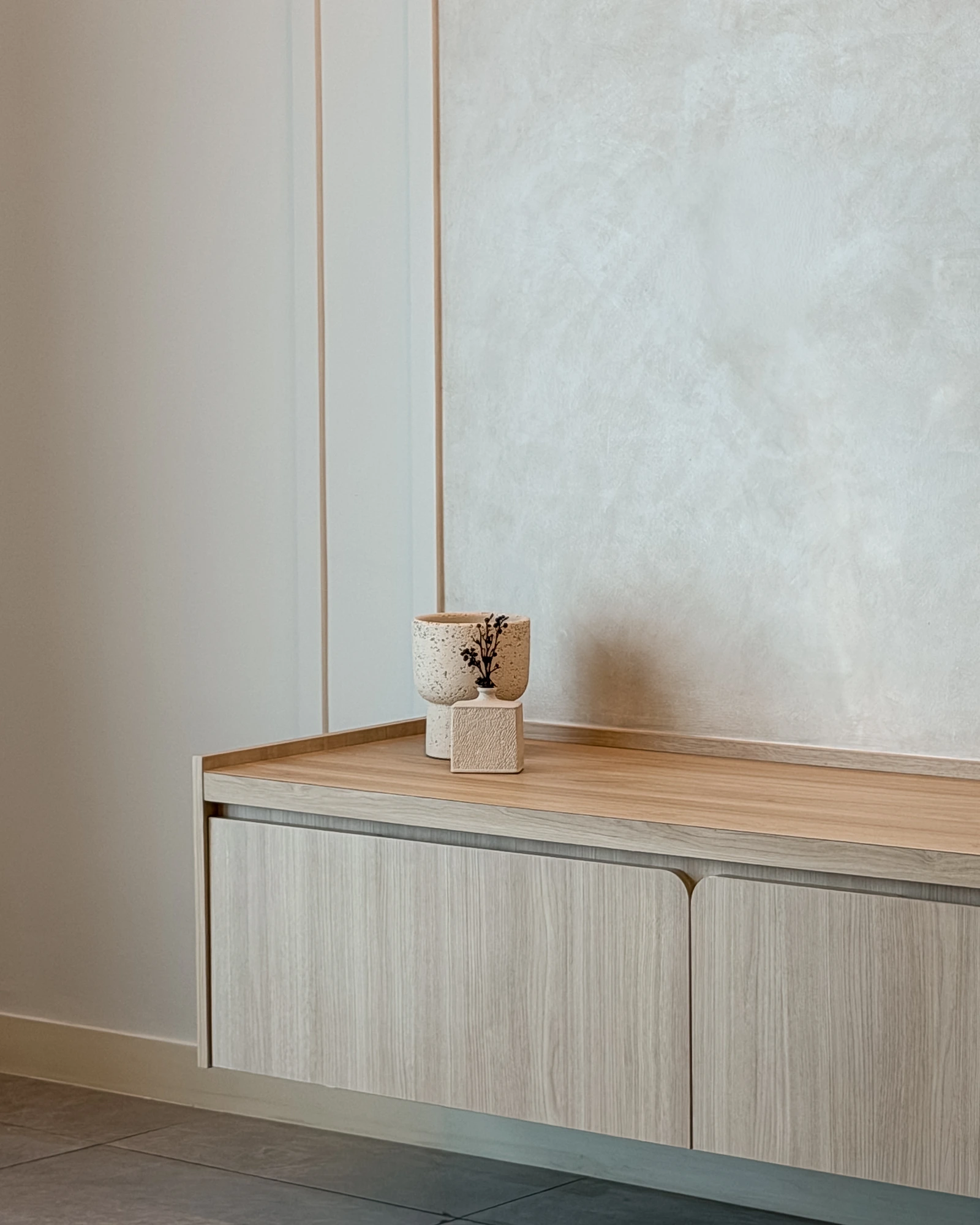 Close-up of a floating wood TV console with rounded cabinet doors and textured feature wall at Ooak Suites, Mont Kiara