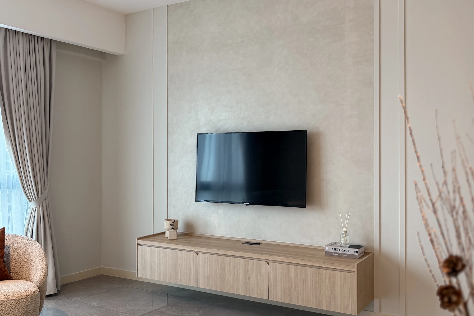 Modern beige TV feature wall with textured finish and floating wood TV console in a neutral living room in Ooak Suites, Mont Kiara.