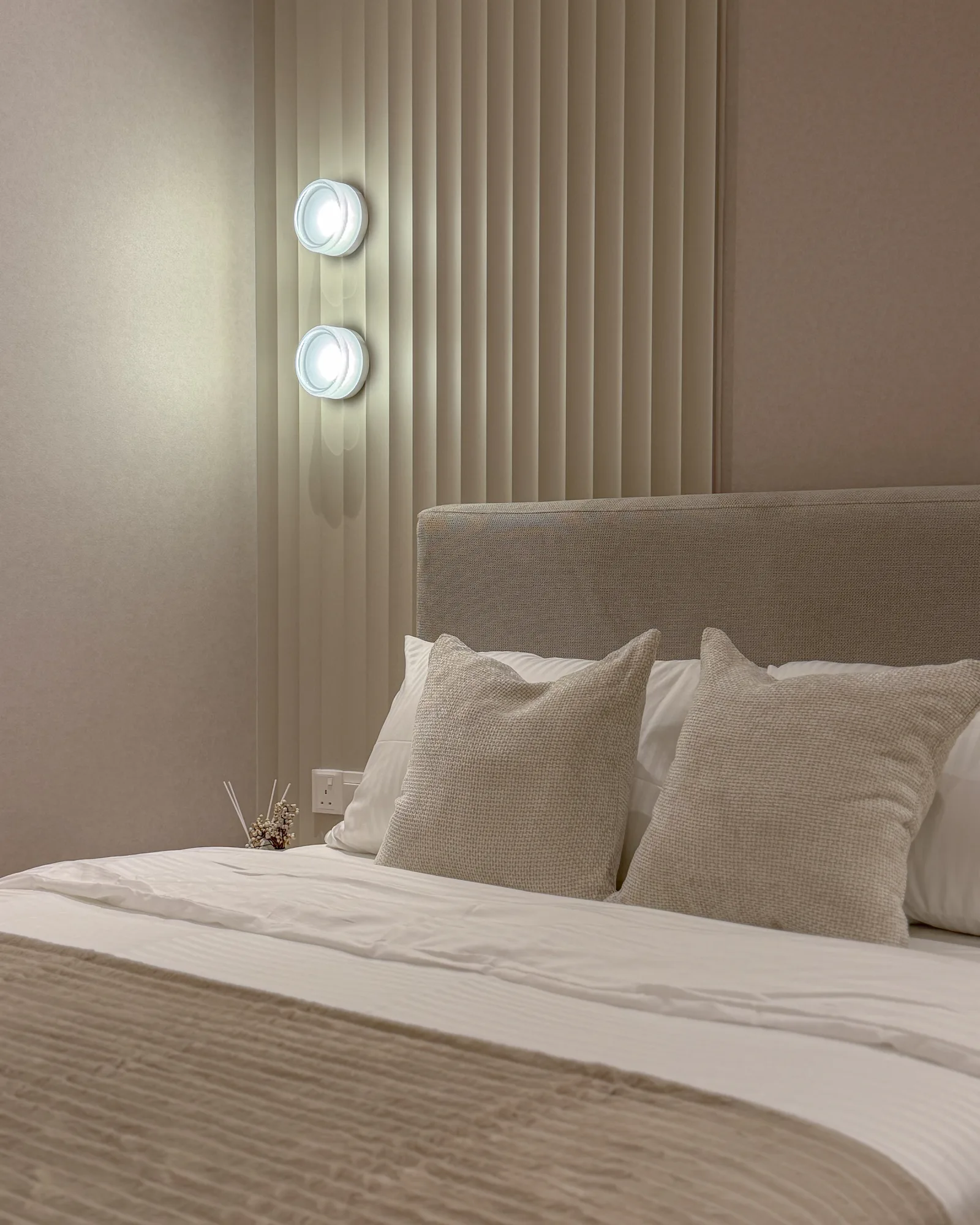 Modern bedroom interior design at TRX Residences, Kuala Lumpur, featuring a textured upholstered headboard, neutral bedding, soft cushions and vertical wall panelling with integrated lighting.