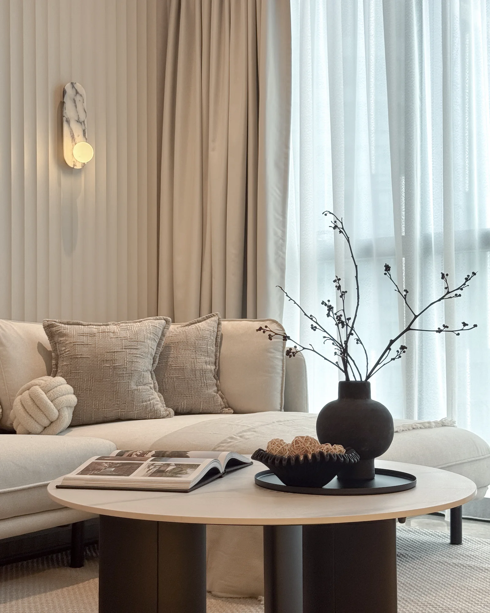 Modern living room interior design at TRX Residences, Kuala Lumpur, featuring a neutral sofa, textured cushions, sheer curtains, warm lighting and a sculptural coffee table arrangement.