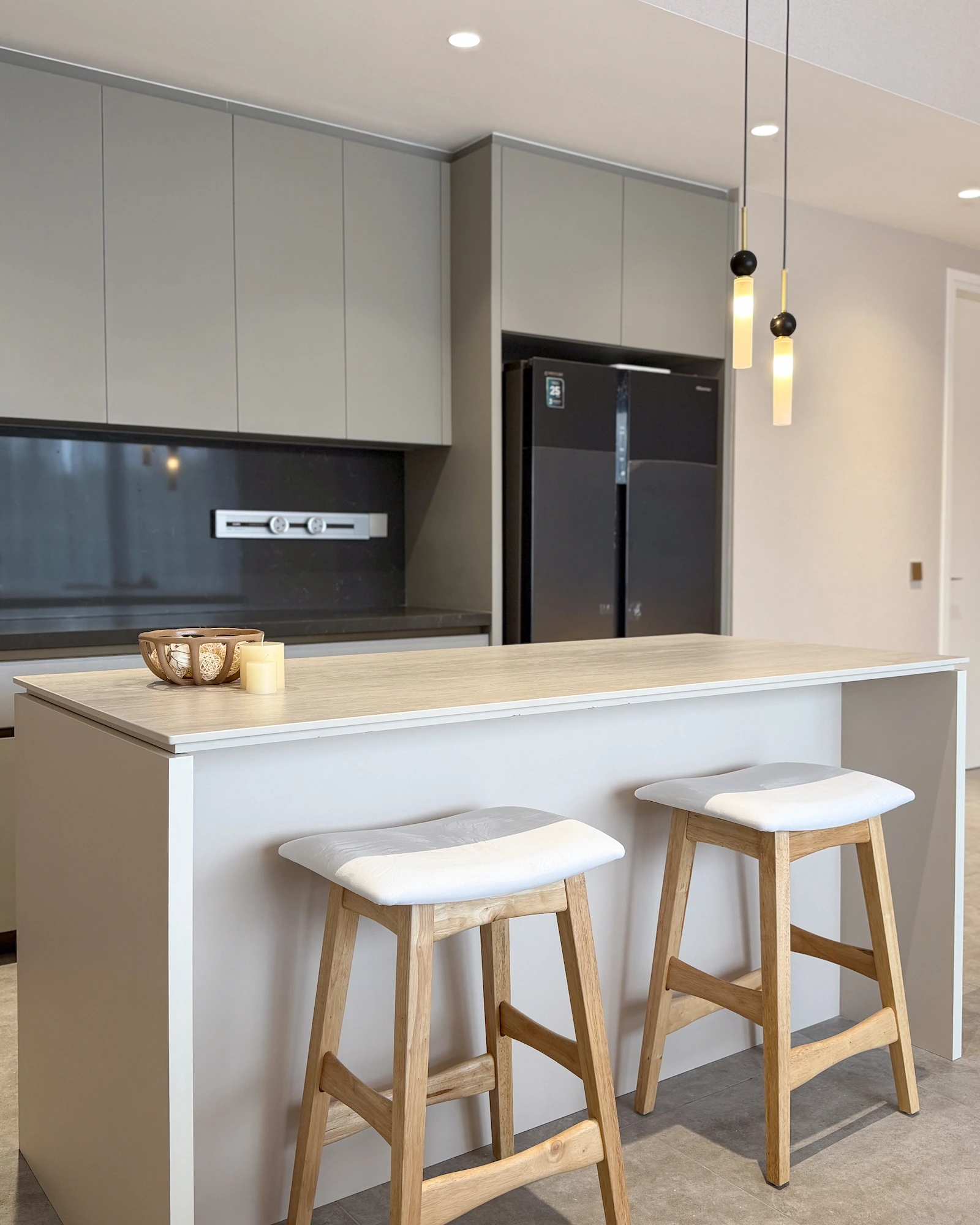 The Muji Apt kitchen in Kuala Lumpur with a minimalist kitchen island, light wood countertop, grey cabinetry and bar stools.