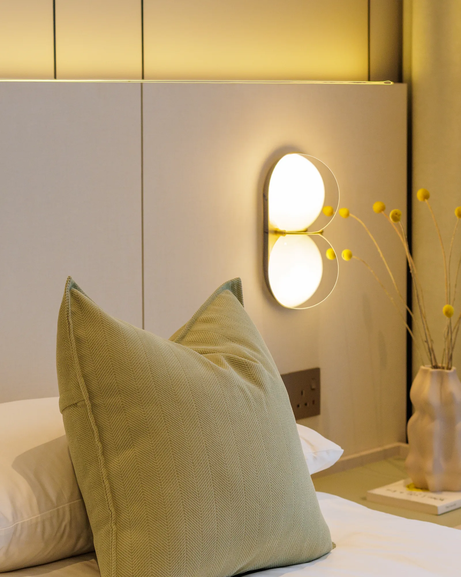 The Radius bedroom detail featuring a textured green accent cushion, sculptural wall light, and bedside styling in a soft neutral palette.