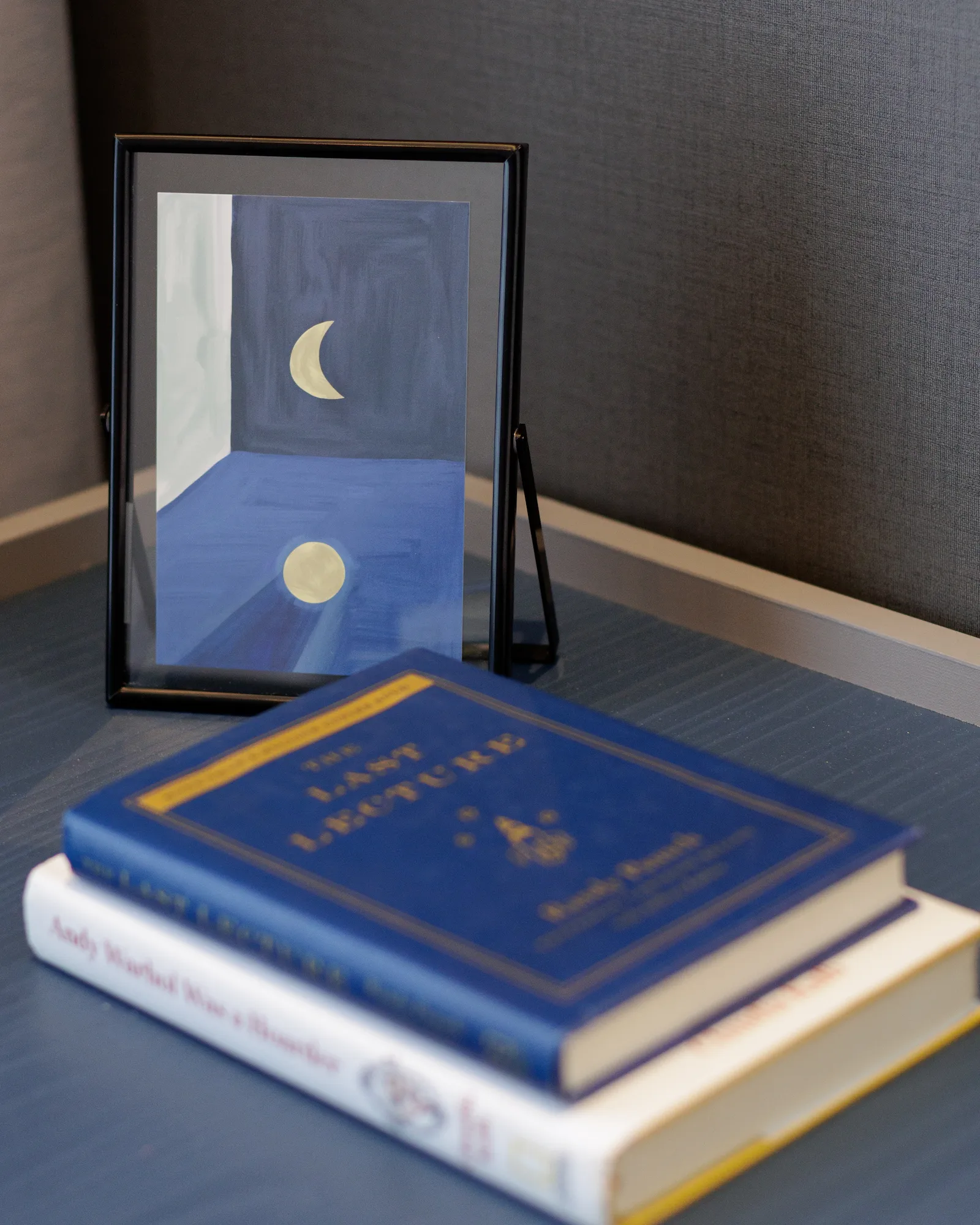 The Radius bedroom bedside table styled with art books and a framed blue artwork against a textured upholstered headboard.