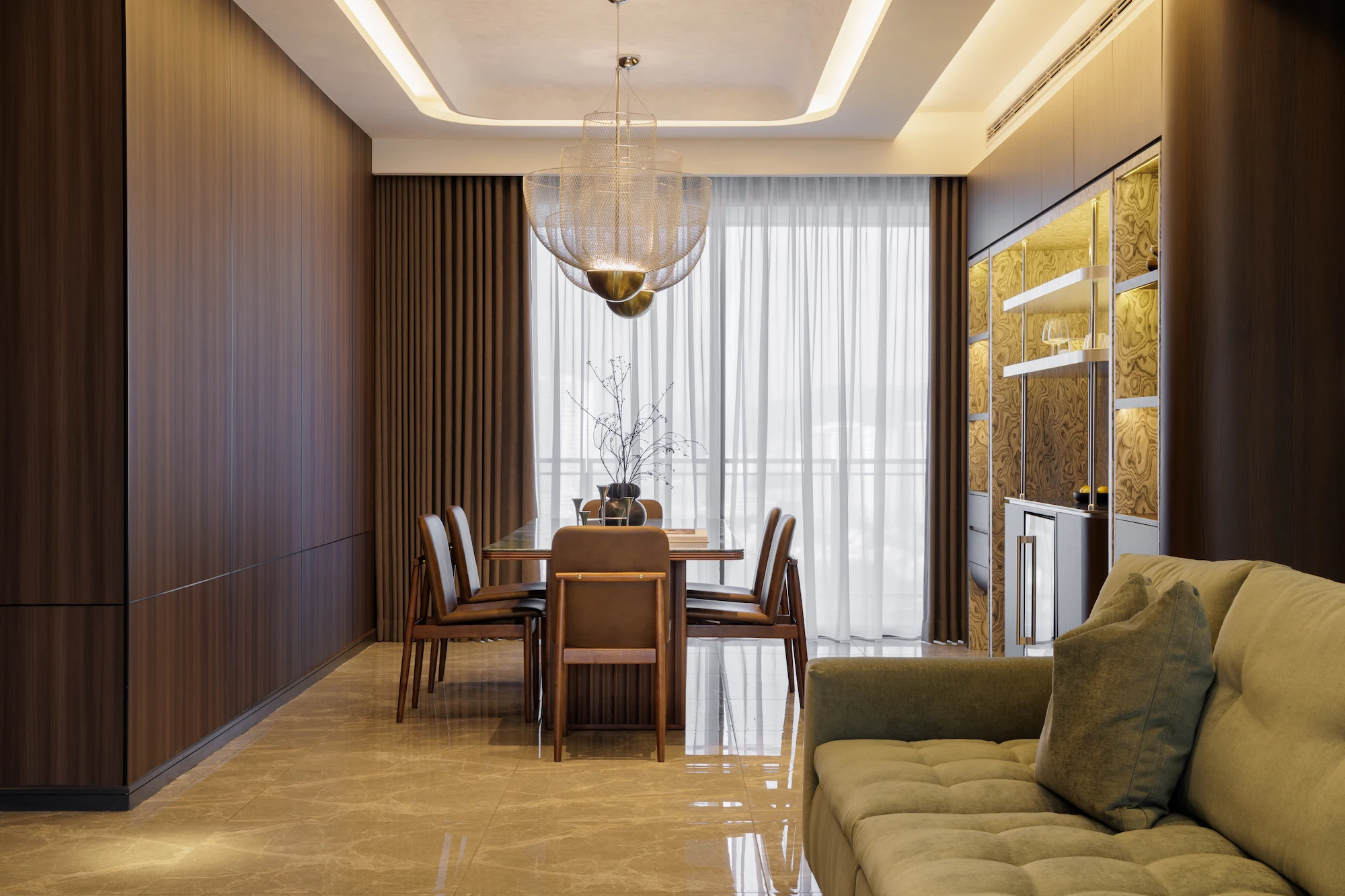 The Radius open-plan living and dining area featuring a dark wood TV wall, concealed hallway doors, warm marble flooring, and a custom dining area with leather chairs.