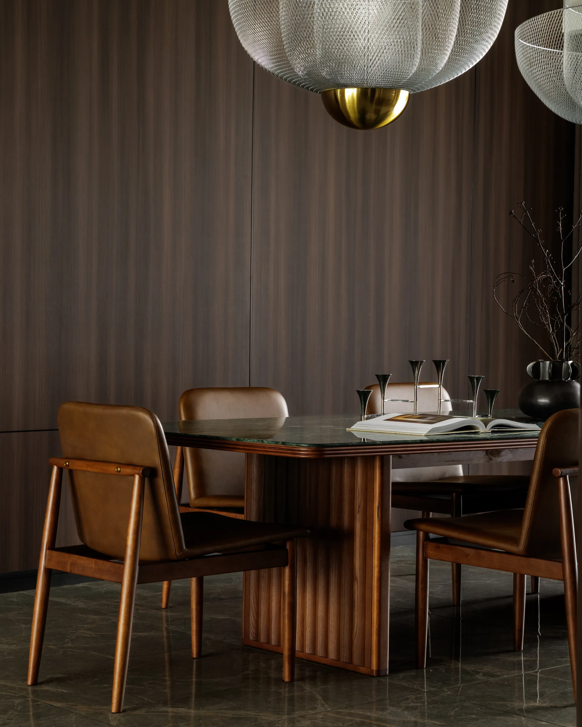 The Radius dining room featuring a dark wood wall, sculptural pendant lights, a fluted wood dining table with leather chairs, and marble flooring.