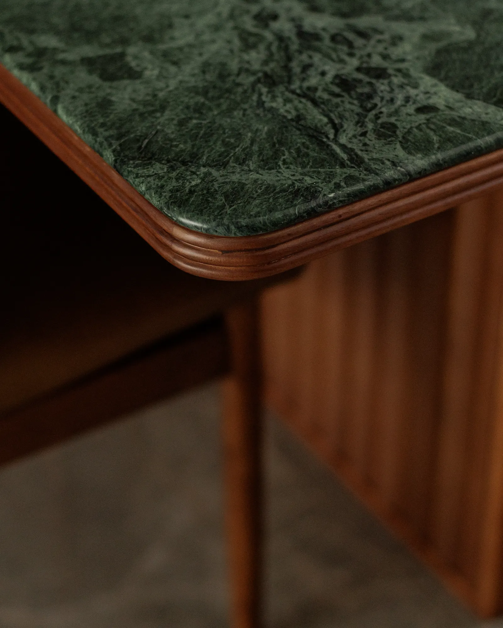 Close-up of The Radius dining table showing the rounded green marble edge and detailed walnut woodwork.