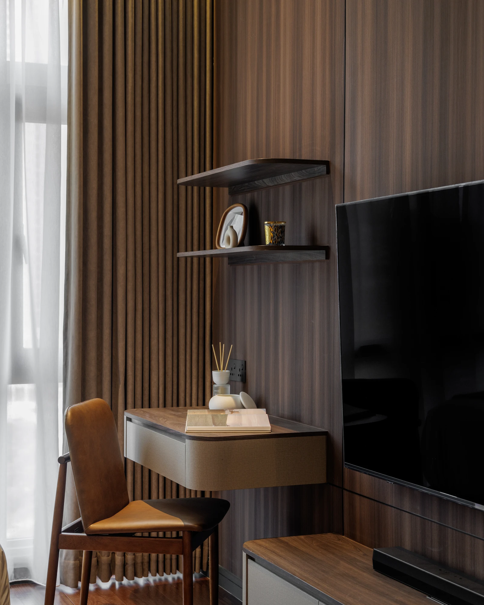 The Radius bedroom study nook featuring a floating wood desk, leather chair, open display shelves, and integrated TV cabinetry.