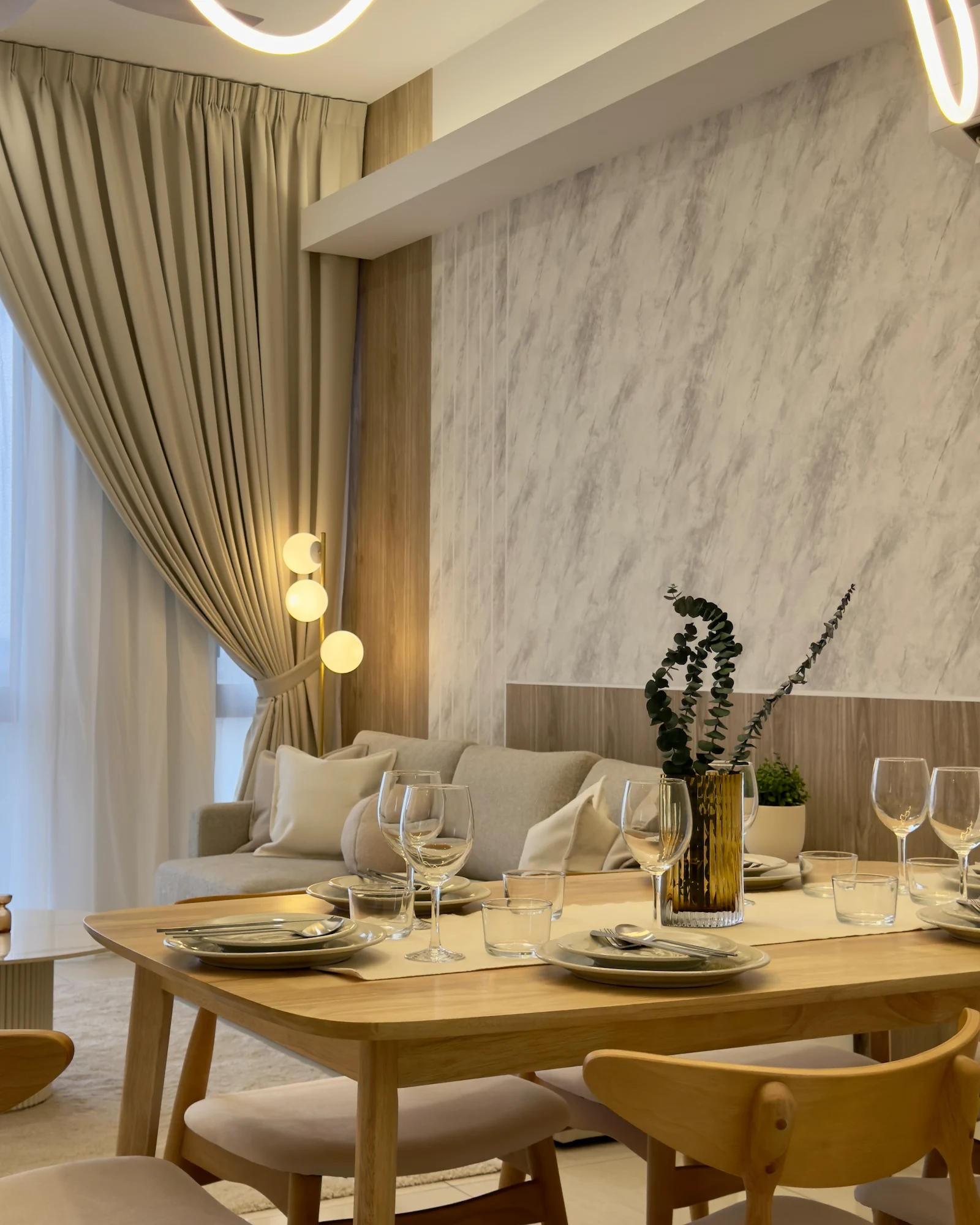Modern apartment living and dining area with warm wood accents, marble-effect feature wall, beige sofa, dining table and floor-to-ceiling curtains in Sentral Suites, Kuala Lumpur