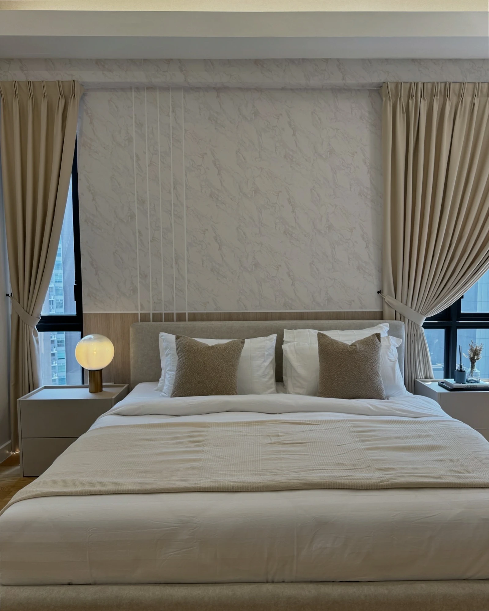 Master bedroom with a warm wood headboard, marble-effect feature wall, built-in bedside tables and full-height curtains in Sentral Suites, Kuala Lumpur.