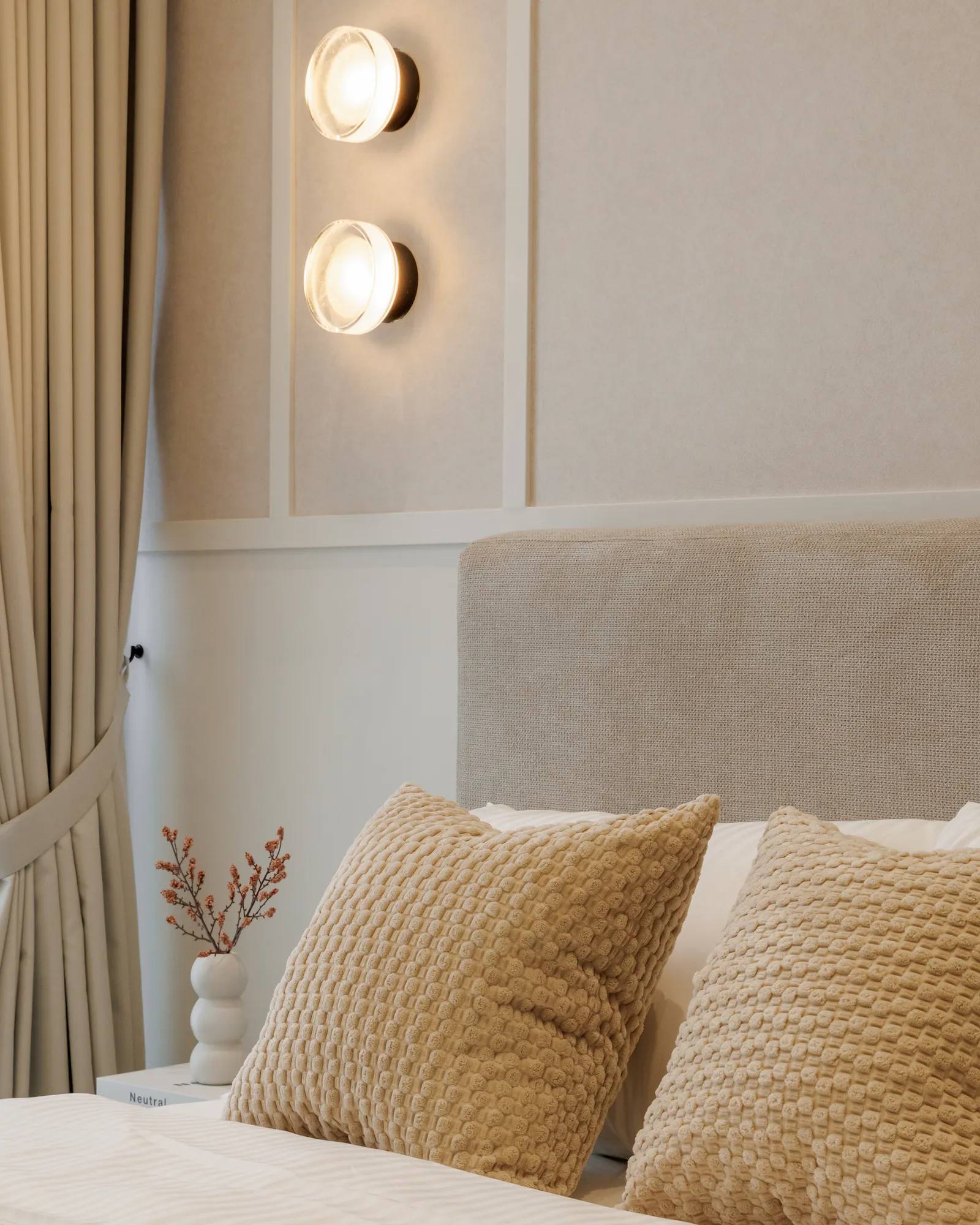 Textured bedroom headboard with warm wall sconces, curtains and neutral cushions