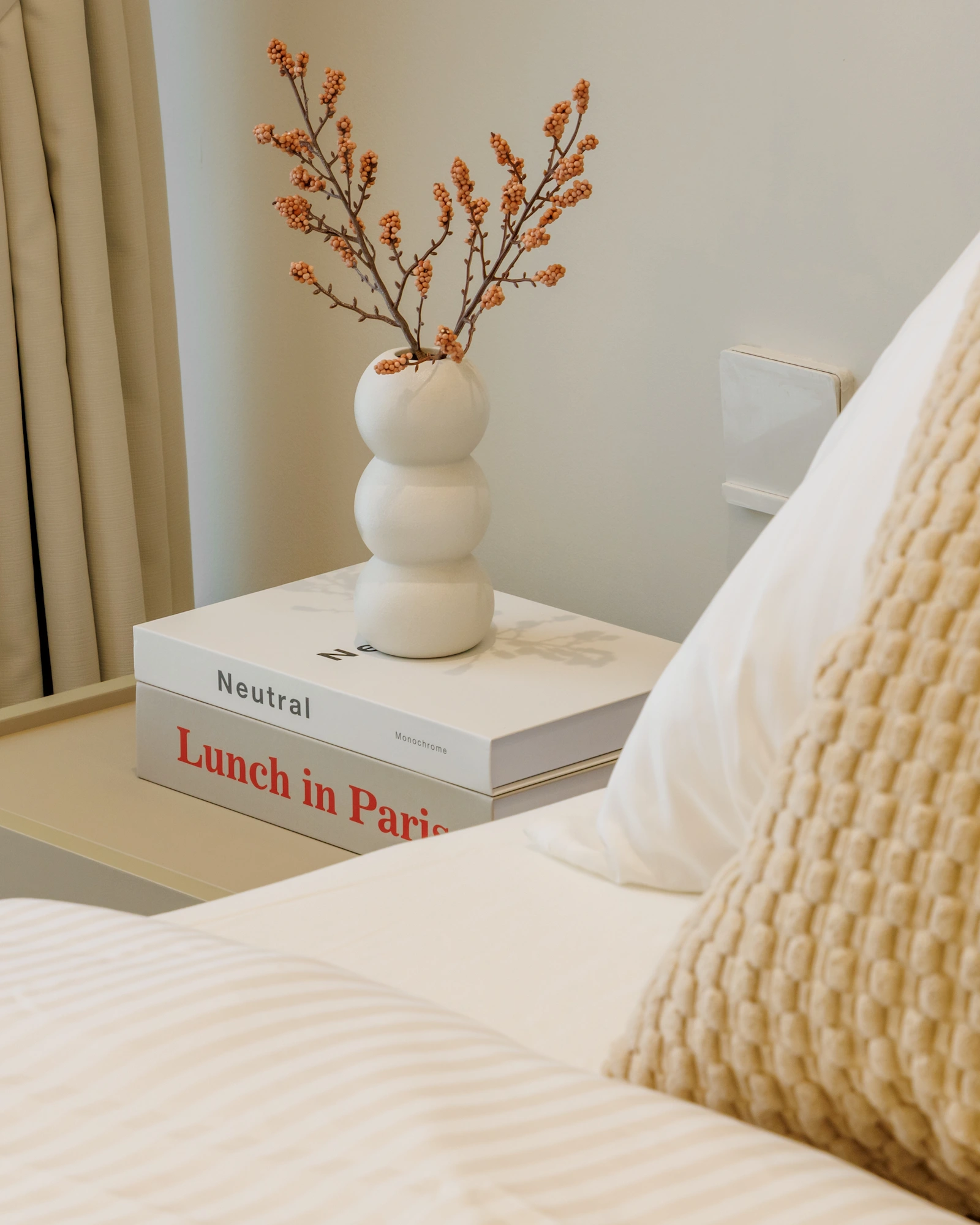 Bedroom bedside table with sculptural white vase, dried branches and layered neutral bedding