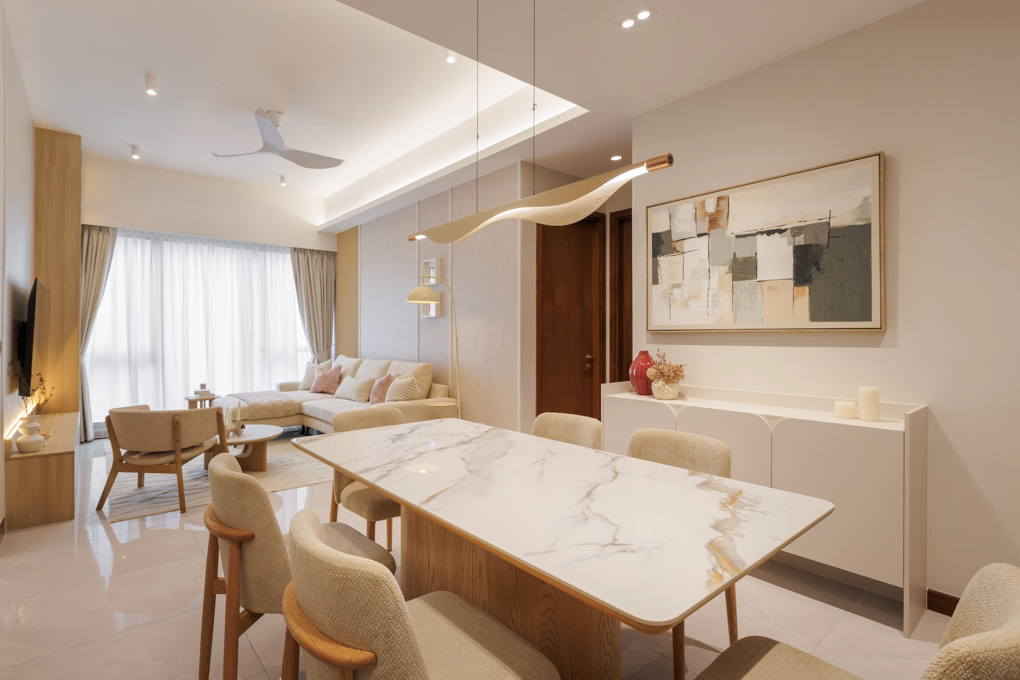 Open-plan dining and living area with marble table, timber furniture and sculptural pendant lighting