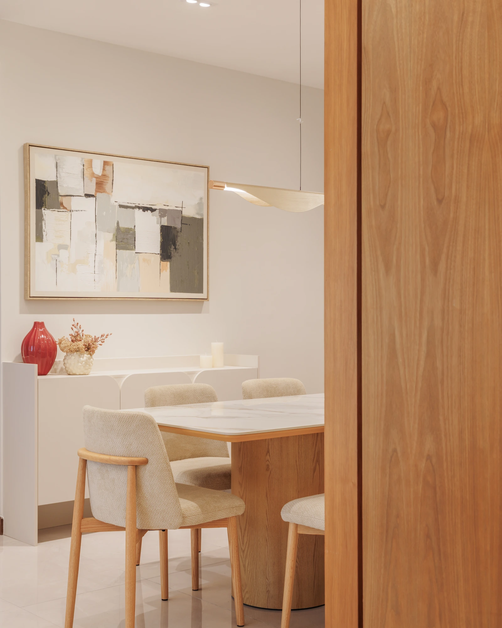 Dining area with marble table, upholstered timber chairs, sculptural pendant light and warm wood door