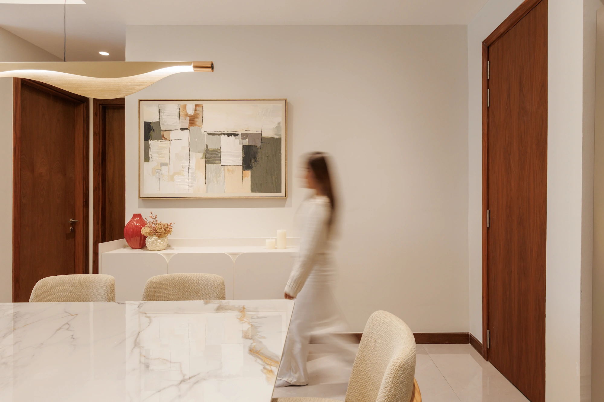 Warm-toned dining area with timber doors, sculptural pendant light, marble dining table and blurred figure