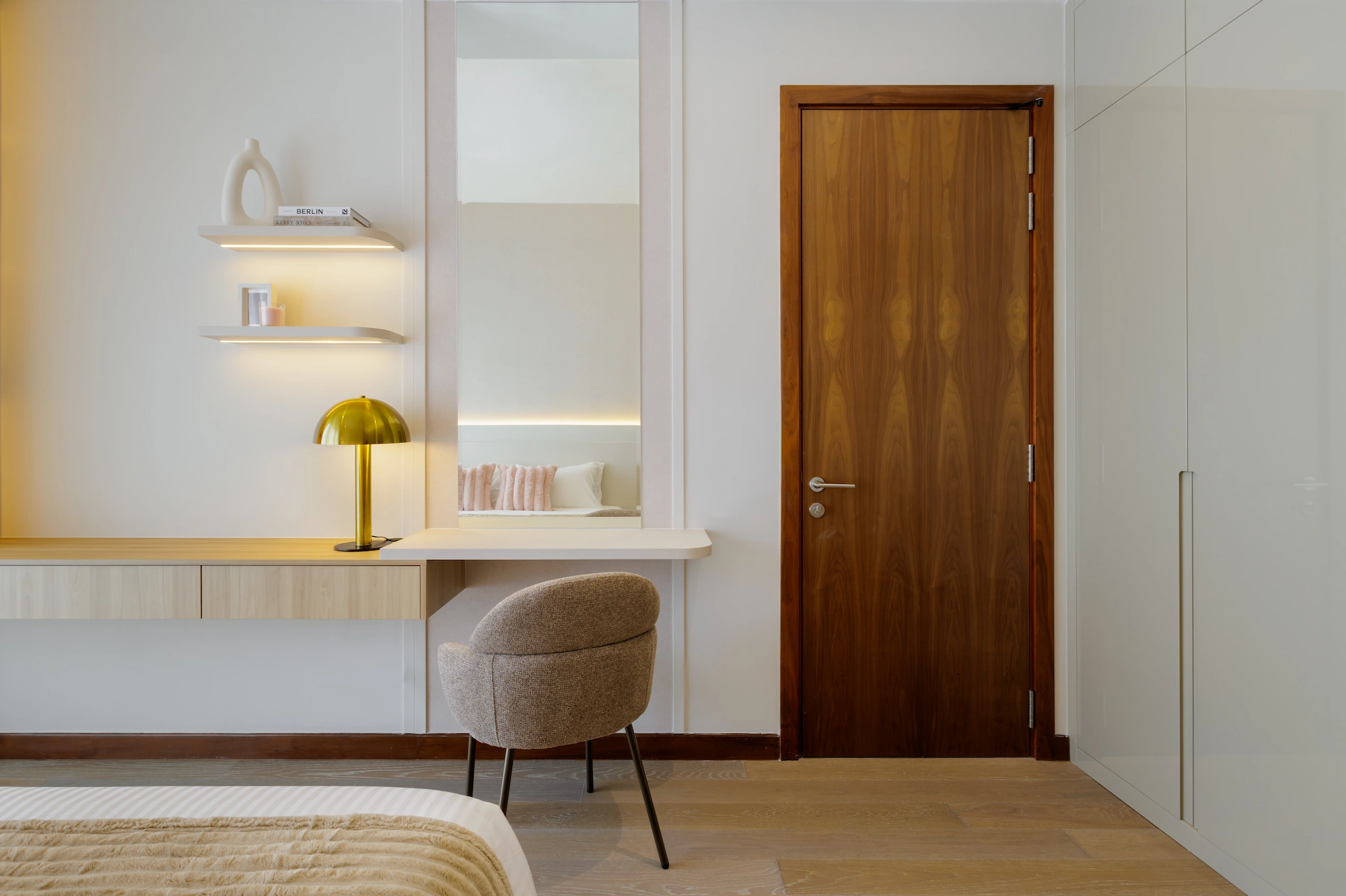 Master bedroom dressing area with built-in vanity, upholstered chair, mirror and warm brass table lamp