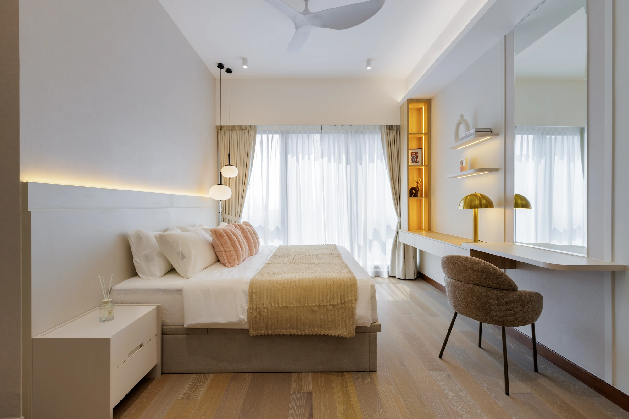 Bright master bedroom with cream bedding, pink cushions, timber flooring and a built-in dressing desk