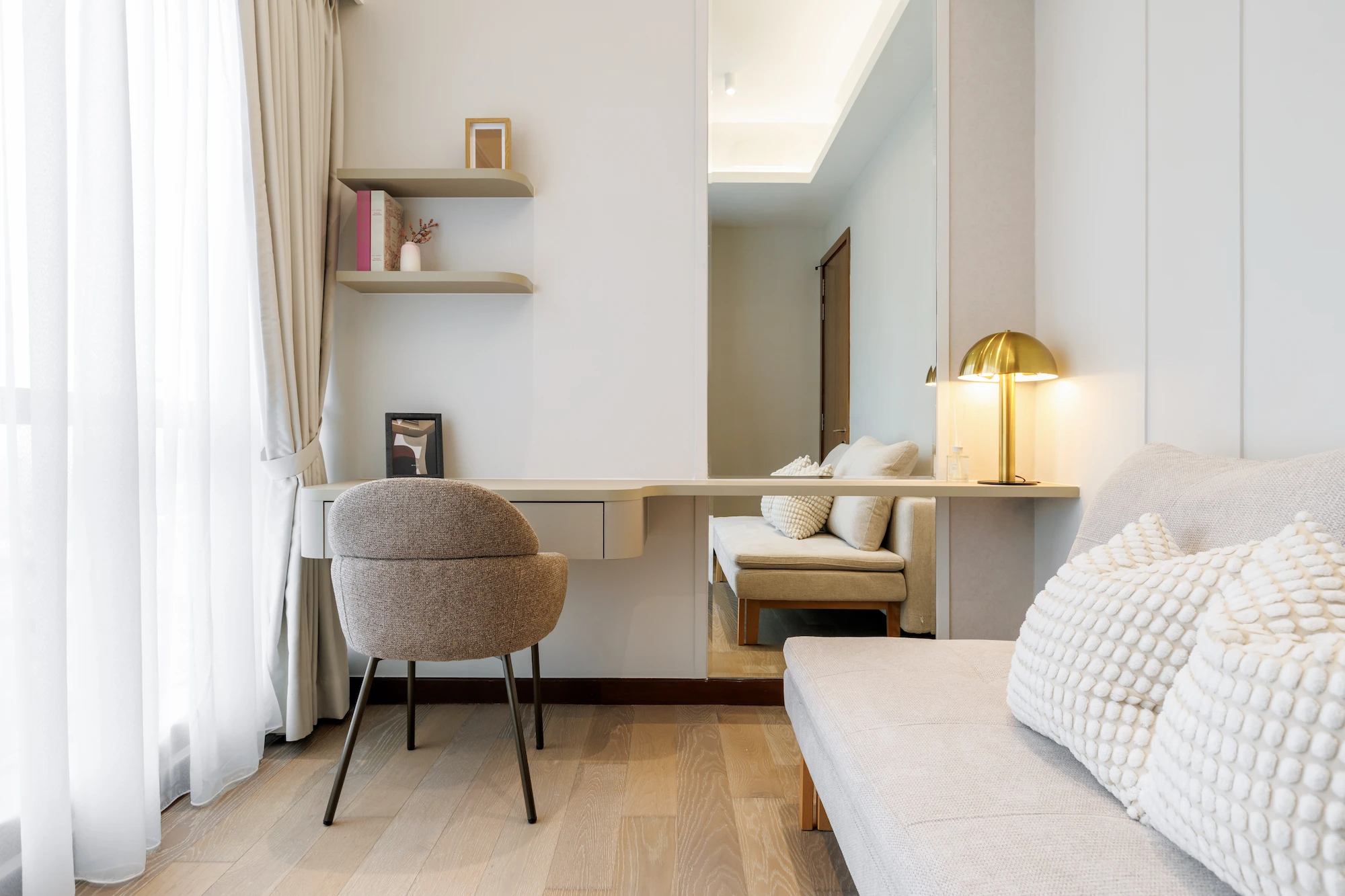 Built-in bedroom desk with upholstered chair, floating shelves and brass table lamp beside a sofa