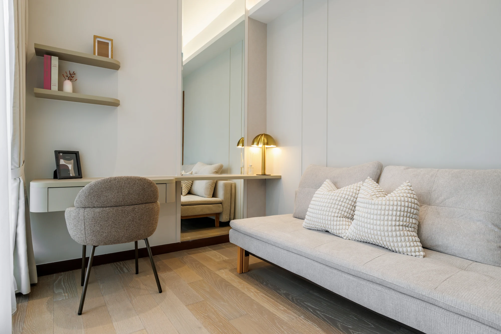 Bedroom study area with built-in desk, upholstered chair, floating shelves and cream sofa